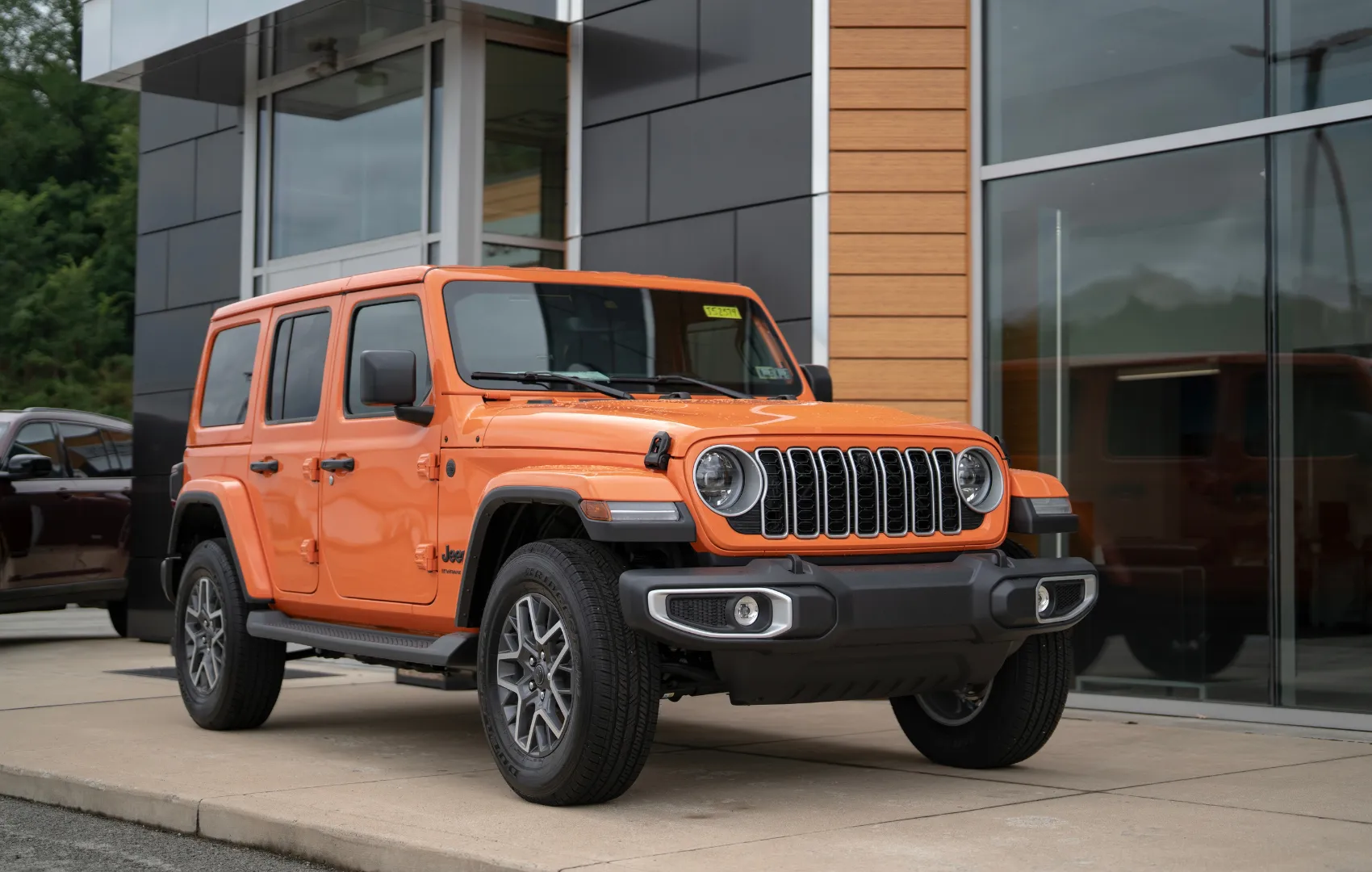 Orange Jeep Wrangler parked outside of front entrance of C. Harper CDJR Mon Valley dealership in Belle Vernon, PA