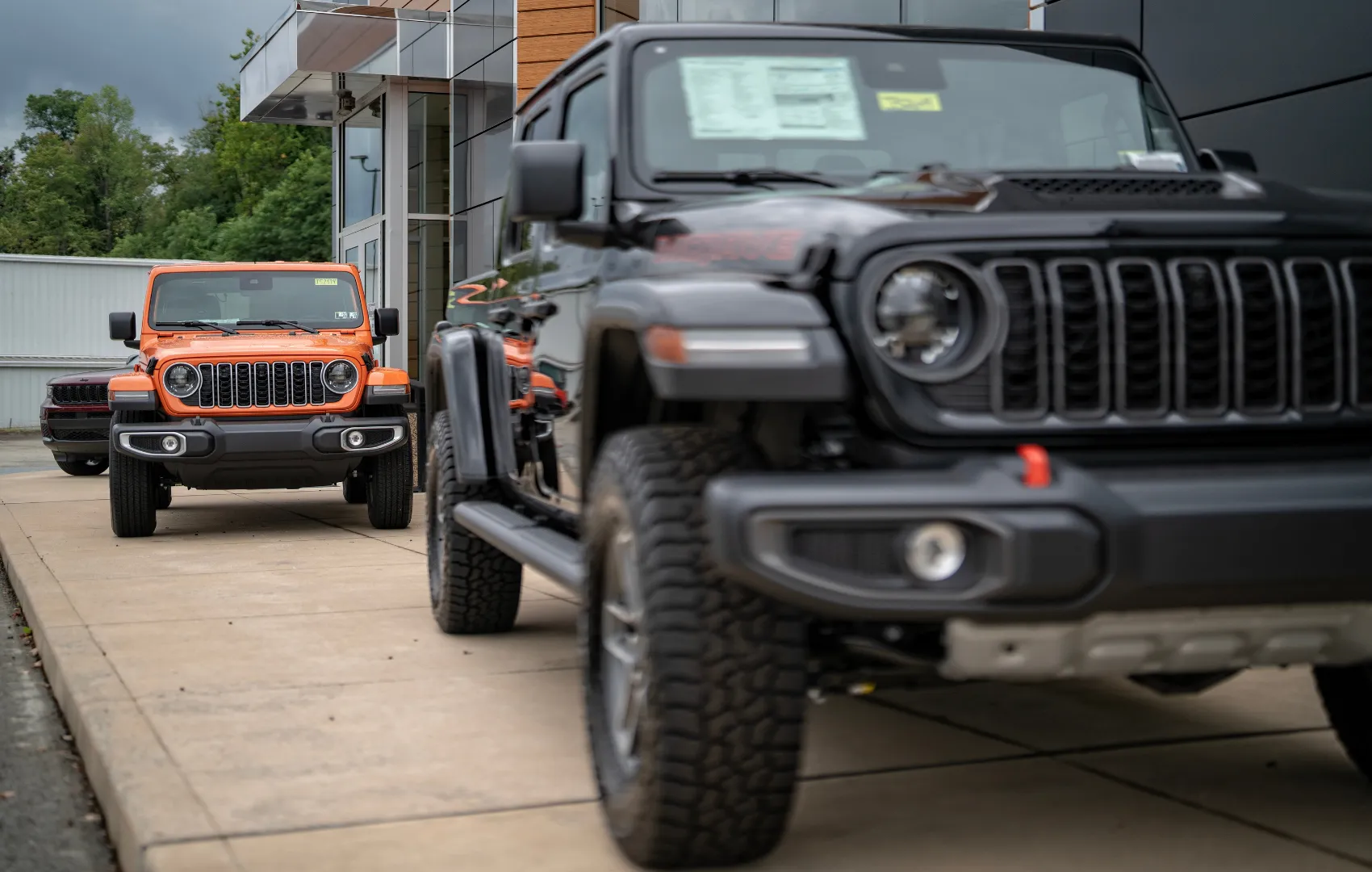 Orange Jeep Wrangler vs. Gladiator in front of C. Harper Mon Valley dealership
